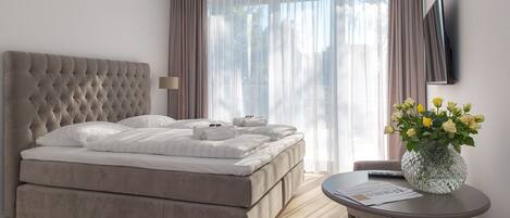A modern hotel room with a large bed, a round table, and a vase of flowers.