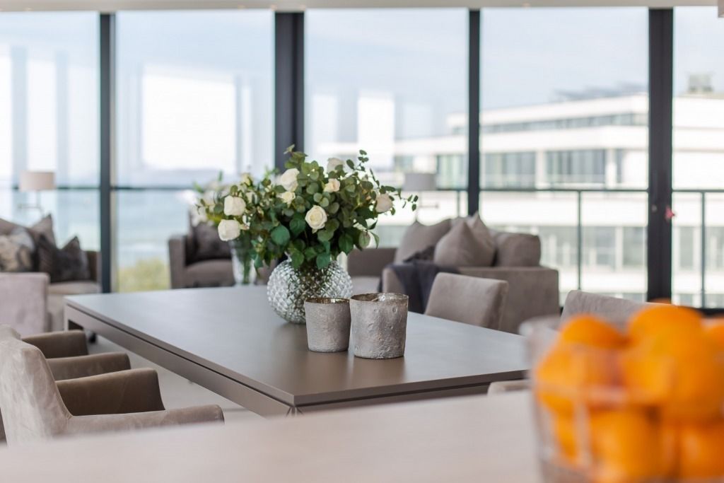 A modern living room with a large window, a dining table, and a view of the city skyline.