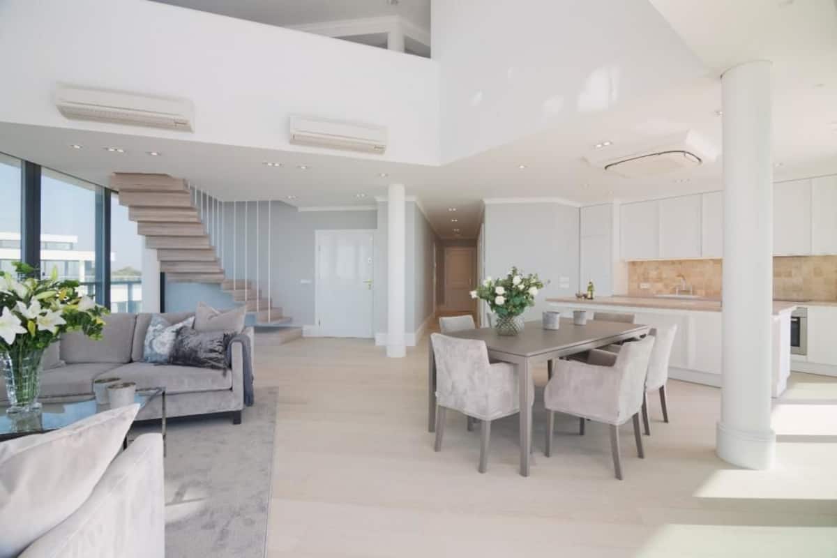 Ampla sala de estar com escada moderna, mesa de jantar com cadeiras e cozinha.