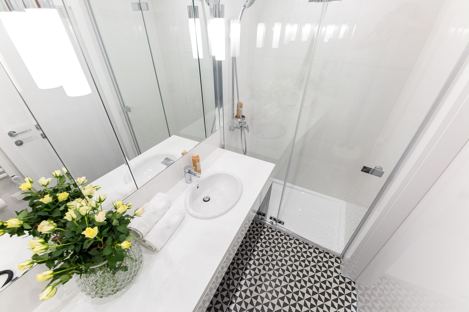 Une salle de bain moderne avec un lavabo blanc, une douche en verre et des carreaux de sol à motifs.
