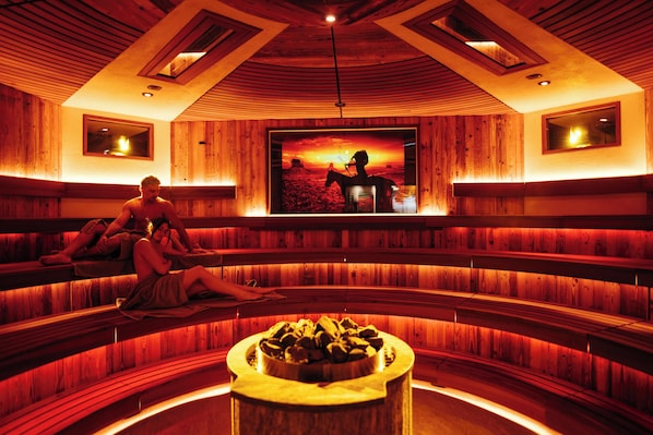 Una sauna con paredes y bancos de madera, un hogar central y un cuadro grande enmarcado que muestra un paisaje desértico.