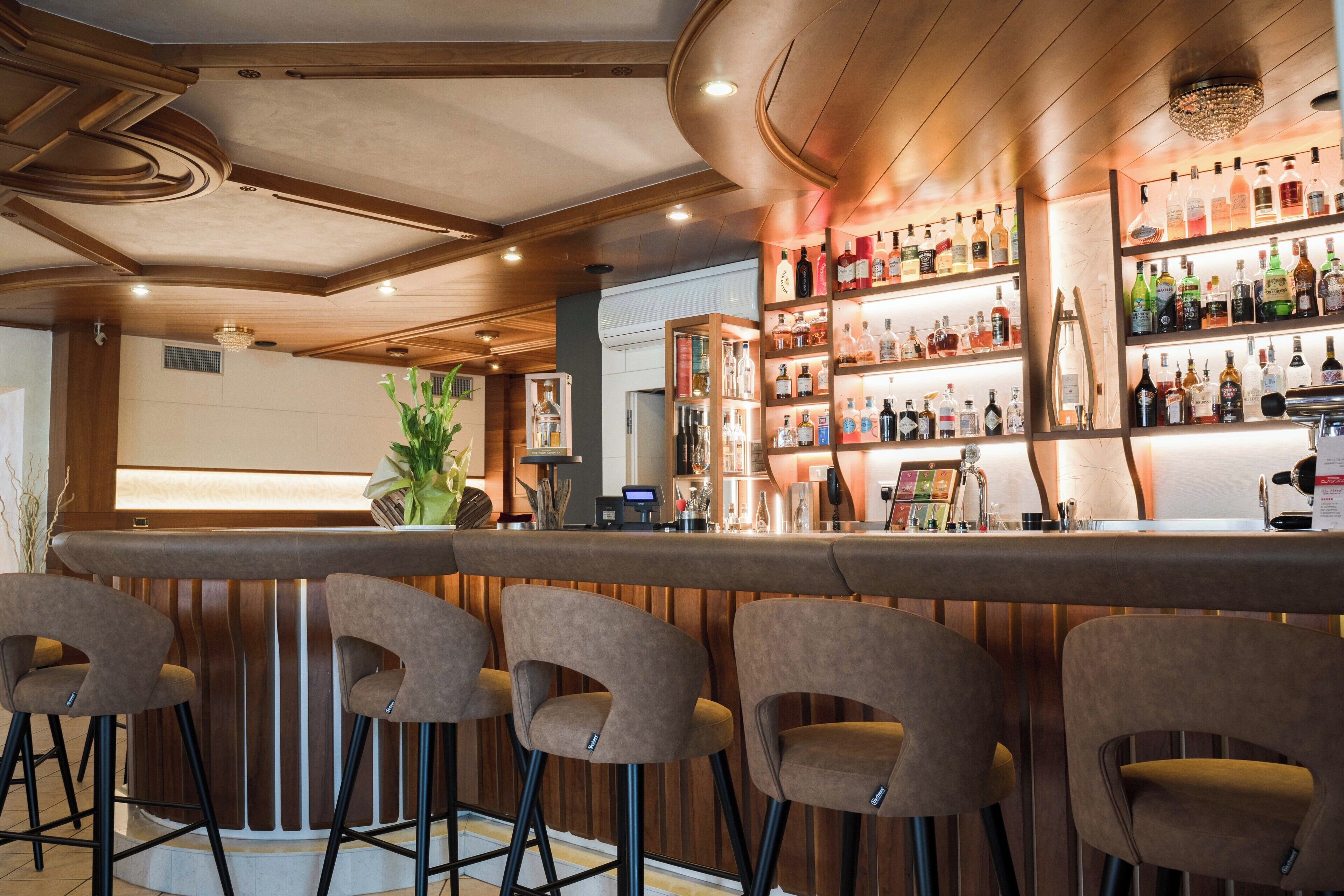 A bar area with wooden bar counters and stools, shelves with various bottles, and a decorative ceiling.