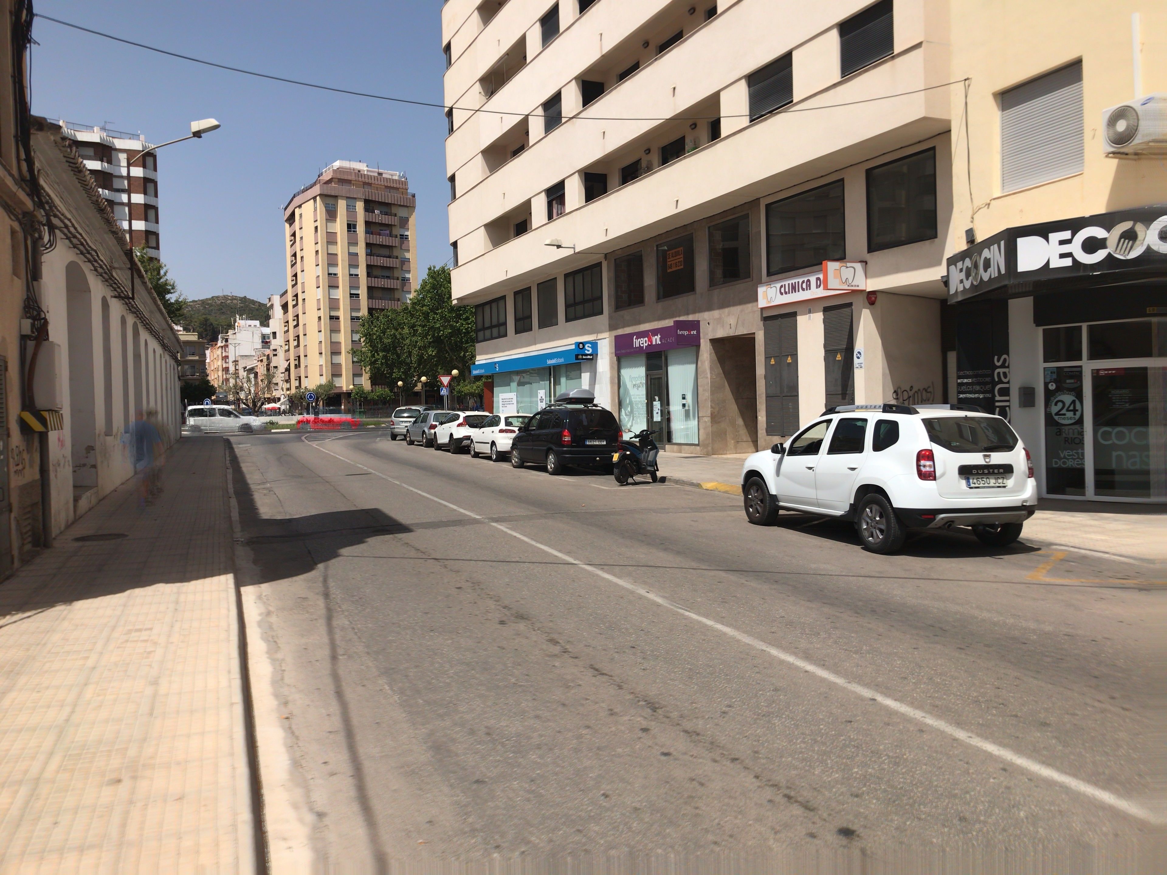 Une rue bordée de voitures garées, une clinique et un immeuble sur lequel on peut lire l’inscription « DECOCIN ».