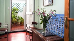 A reception area with a desk, chairs, a vase with flowers, a fish wall art, and a door leading to a balcony with plants. - Hostal Tropical (Oliva)