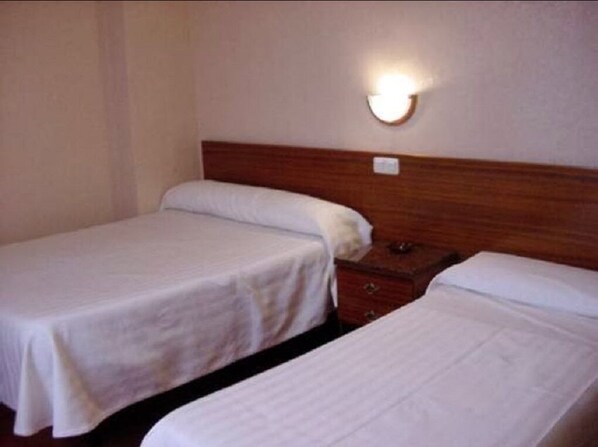 A hotel room with two single beds, a wooden headboard, a nightstand, and a wall-mounted light fixture. - Hostal Tropical (Oliva)