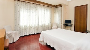 A hotel room with a bed, a desk with a chair, a television, and a wooden door. - Hostal Tropical (Oliva)