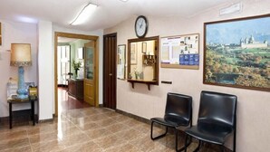A reception area with a tiled floor, two black chairs, a clock, a framed mirror, and a bulletin board. - Hostal Tropical (Oliva)