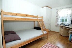 A bunk bed in a room with a wooden desk, a window with curtains, and a radiator.