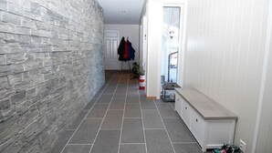 A narrow hallway with a stone wall on one side and a white wall on the other. There is a coat rack with a few items hanging on it, and a small table with a plant and a red object on it. - Solferie Holiday Home - Korsvikkilen (Kristiansand)
