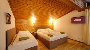 A room with two beds, wooden ceiling, and a wall-mounted TV labeled "NETFLIX".