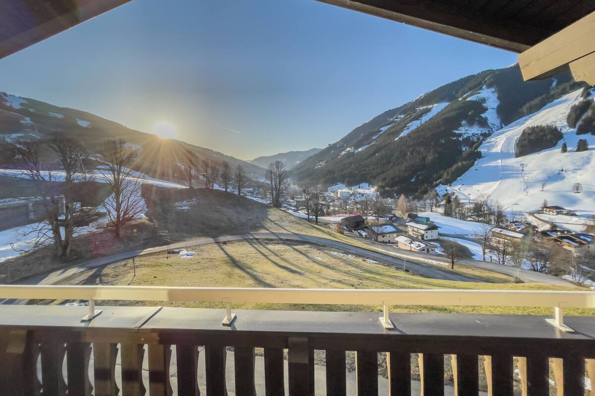 A view from a balcony overlooking a snow-covered valley with a clear sky and the sun shining.