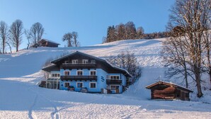 A snow-covered landscape with a large blue house and a smaller wooden structure.
