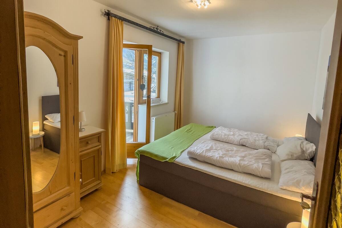 A bedroom with a bed, a wardrobe, a small bedside table, and a window with curtains.