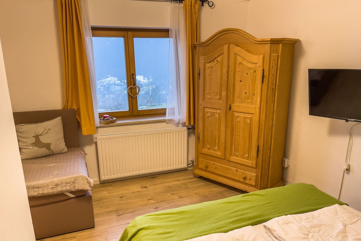 A bedroom with a bed, a dresser, a radiator, a window with curtains, and a television.
