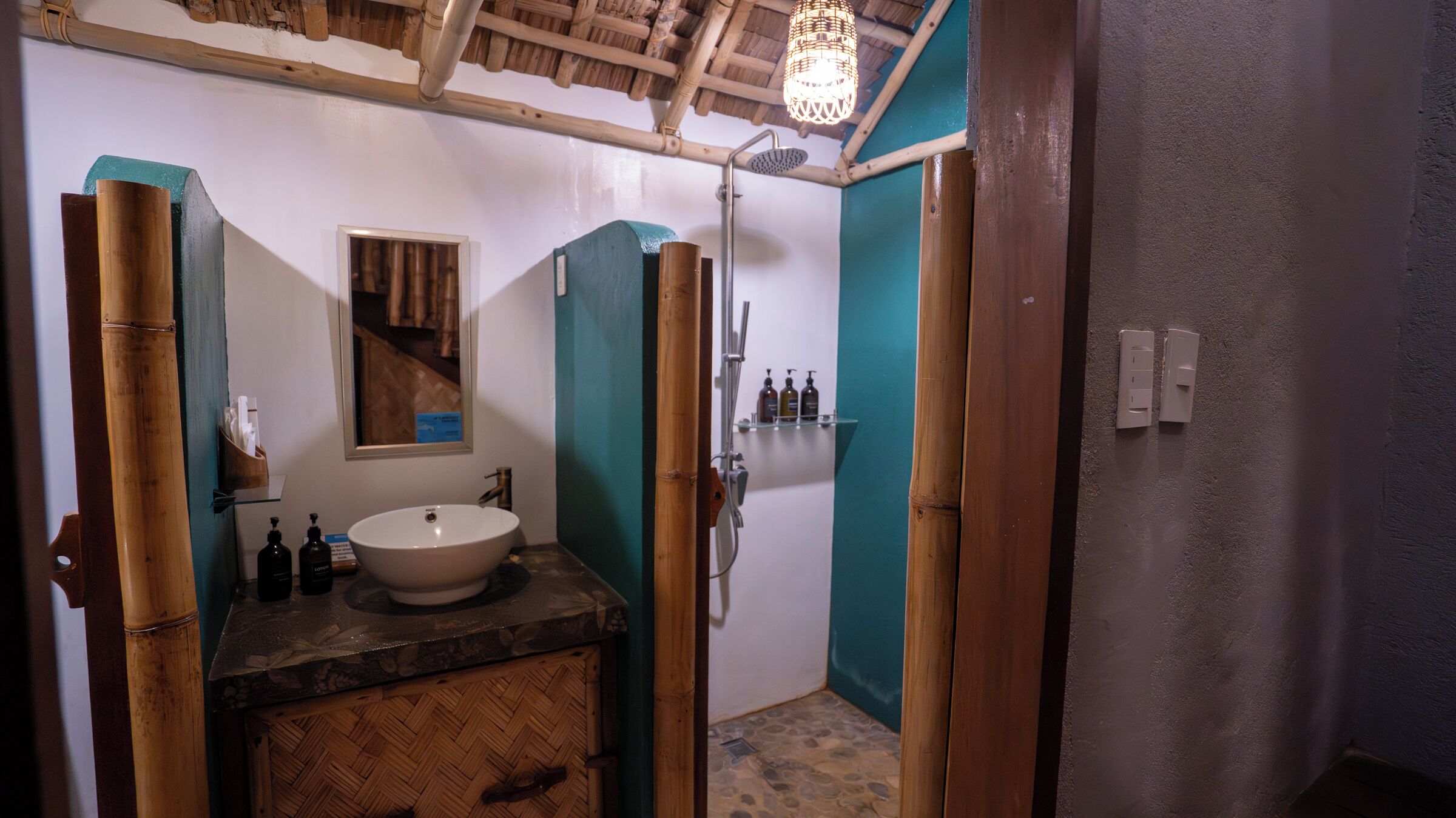 A bathroom with a wooden vanity, a large sink, a mirror, a shower, and a hanging light fixture.