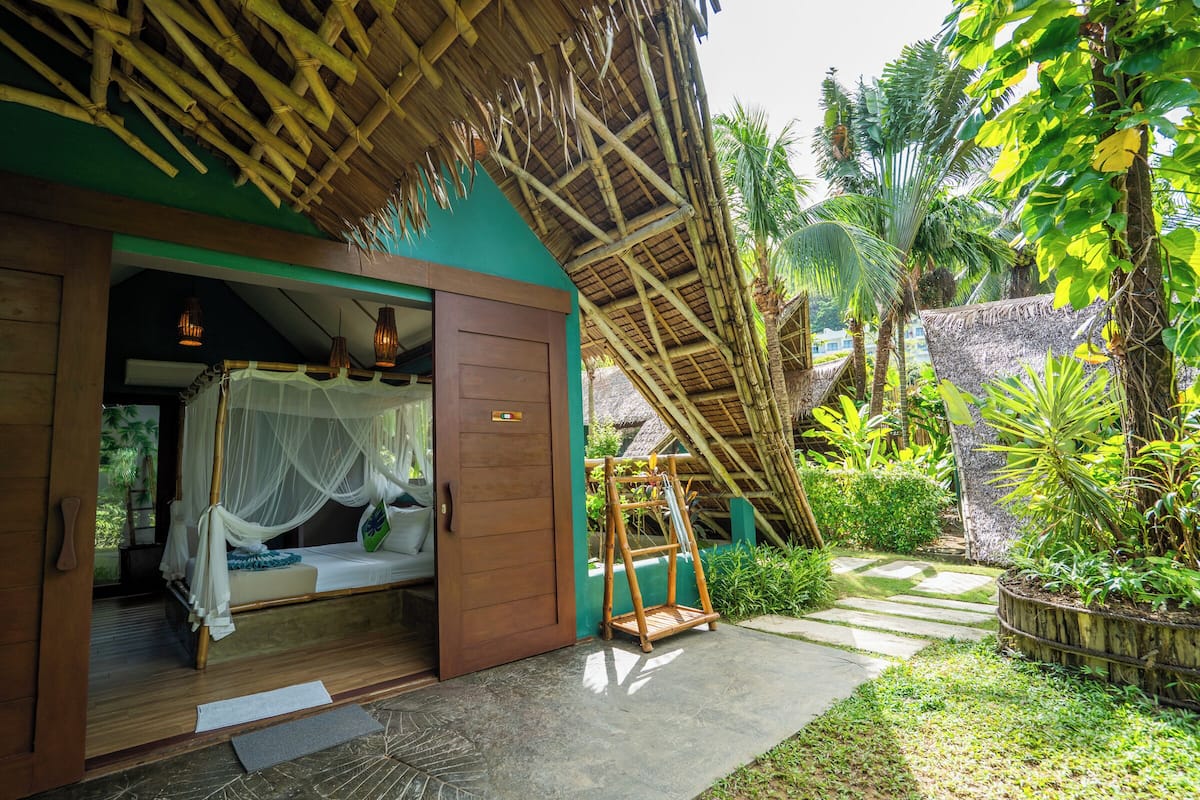 A room with a bed, a wooden door, and a thatched roof.