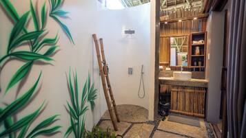 Un baño con una escalera de bambú, ducha y lavamanos con espejo.