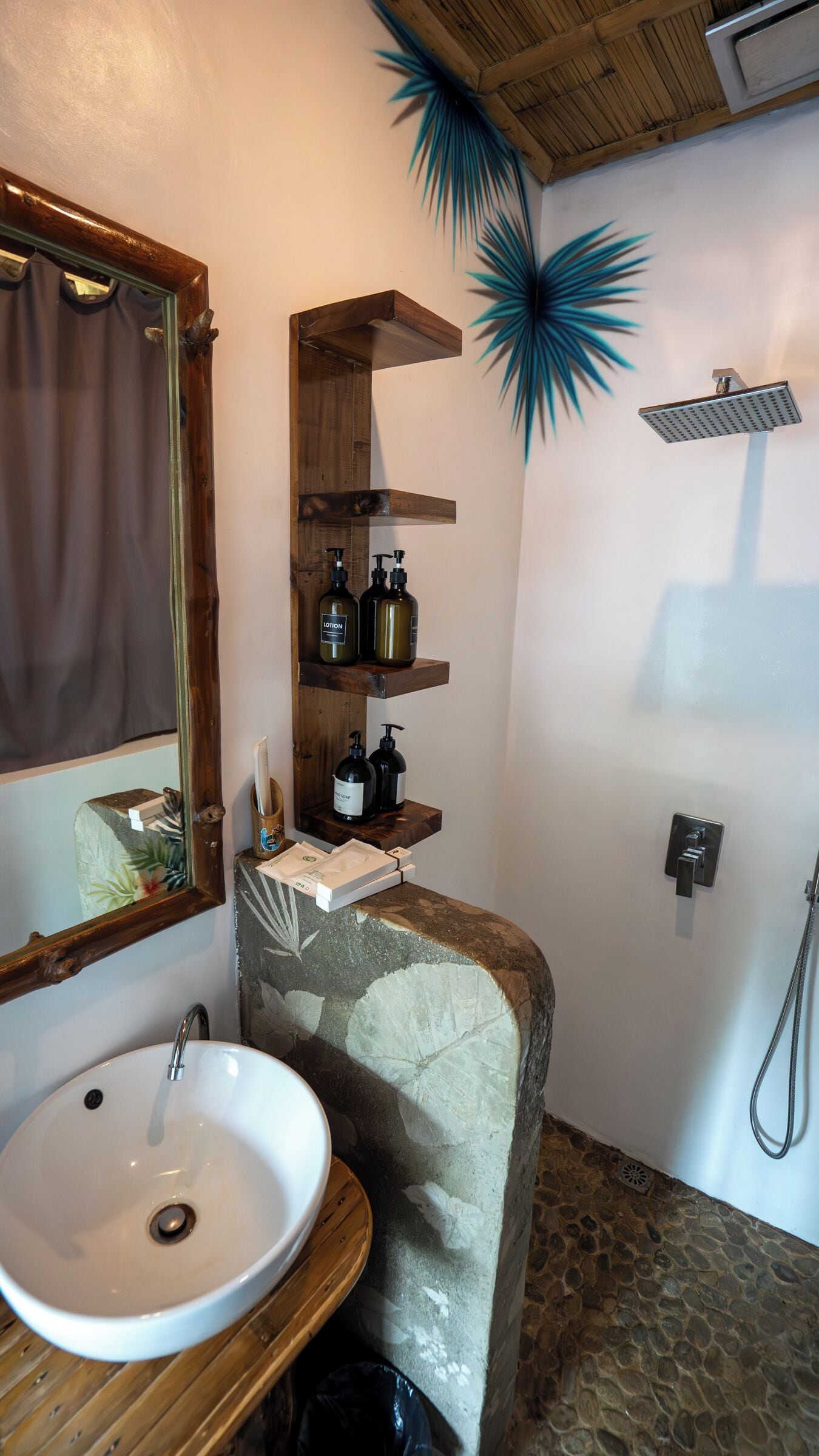 A bathroom with a wooden vanity, a sink, a mirror, a shower, and shelves with toiletries.