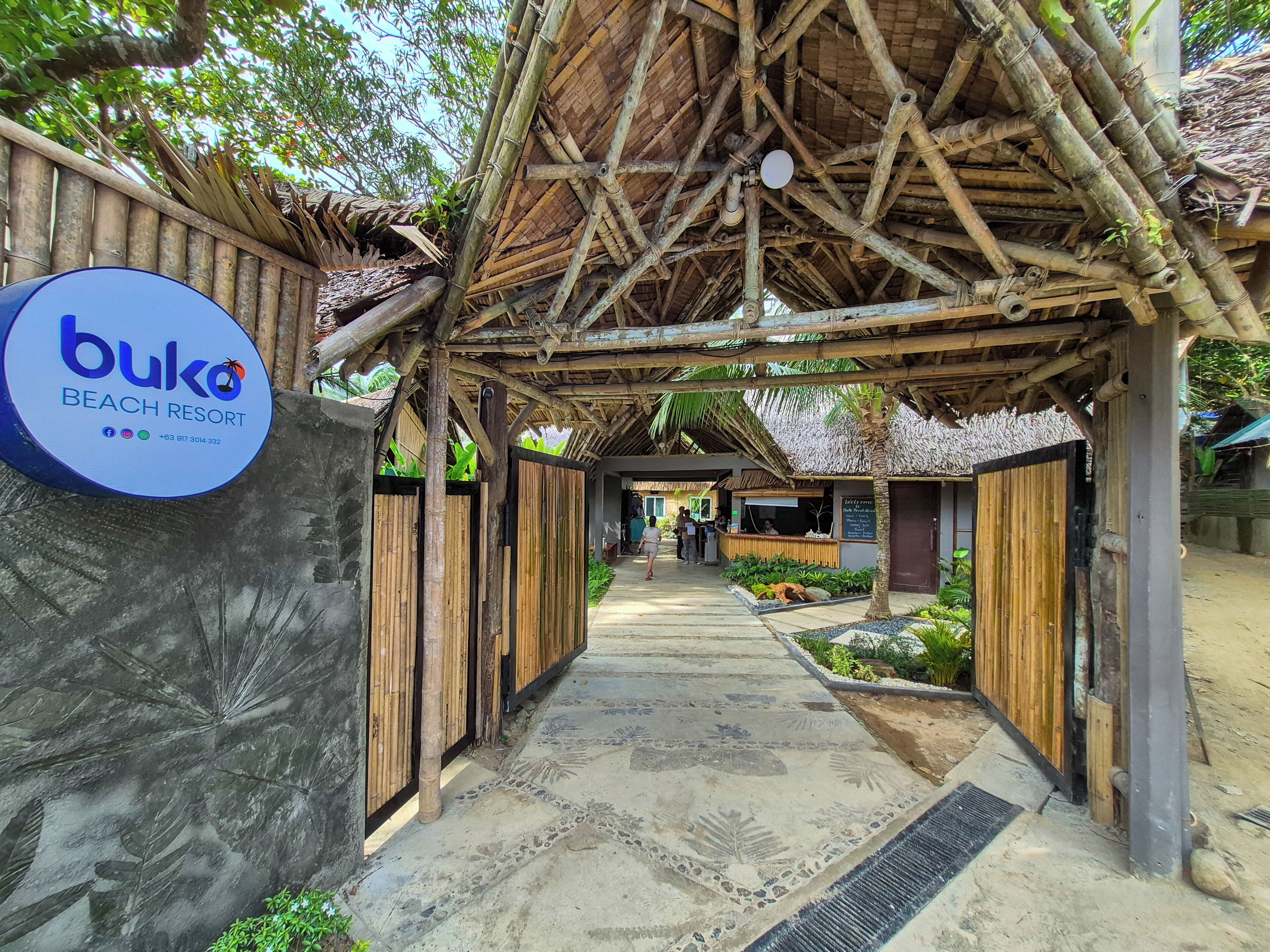 A pathway leading to a beach resort with a bamboo structure and a sign for 'buko beach resort'.
