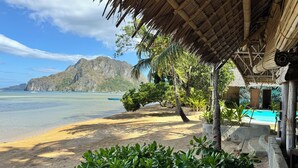 A beach view with a thatched-roof structure, a swimming pool, and lush greenery. - Buko Beach Resort - Adults Only (El Nido)