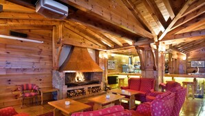 A cozy log cabin interior with a fireplace, wooden furniture, and a bar area.