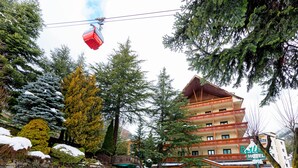 A hotel with a stone wall, a ski lift, and snow-covered trees.