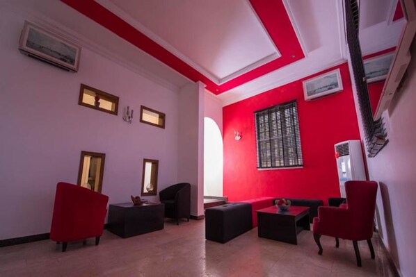A room with red and white walls, a black sofa, a small table, and a window with blinds. - Bates Place Apartments (Lekki)
