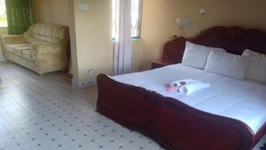 A hotel room with a large bed, a sofa, and a window with curtains.