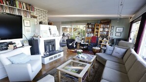 A spacious living room with a fireplace, a bookshelf, a sofa, and a television. - Solferie Holiday Home Vardåsveien (Kristiansand)