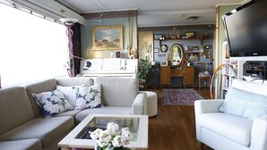 A cozy living room with a sofa, armchair, and coffee table, a television, and a bookshelf filled with books and decorative items. - Solferie Holiday Home Vardåsveien (Kristiansand)