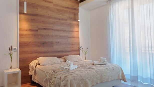 A modern bedroom with a wooden ceiling, a large bed, and a bedside table with a lamp. - Lumiere Rooms - Eja Sardinia (Cagliari)