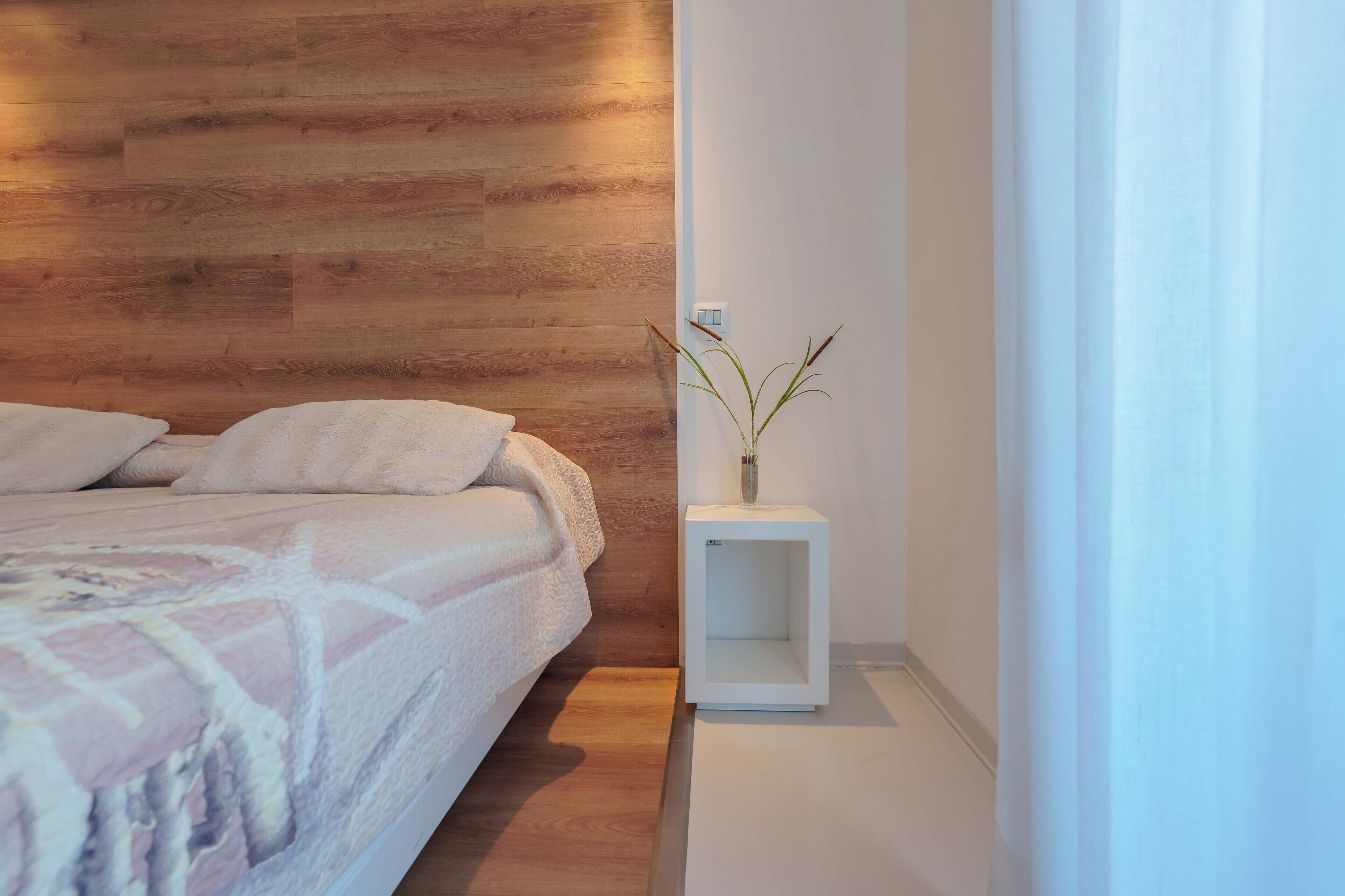 A bedroom with a wooden headboard, a bed with a white blanket, and a bedside table with a plant.