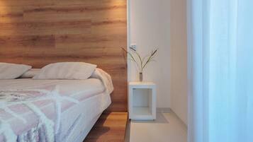 A bedroom with a wooden headboard, a bed with a white blanket, and a bedside table with a plant.