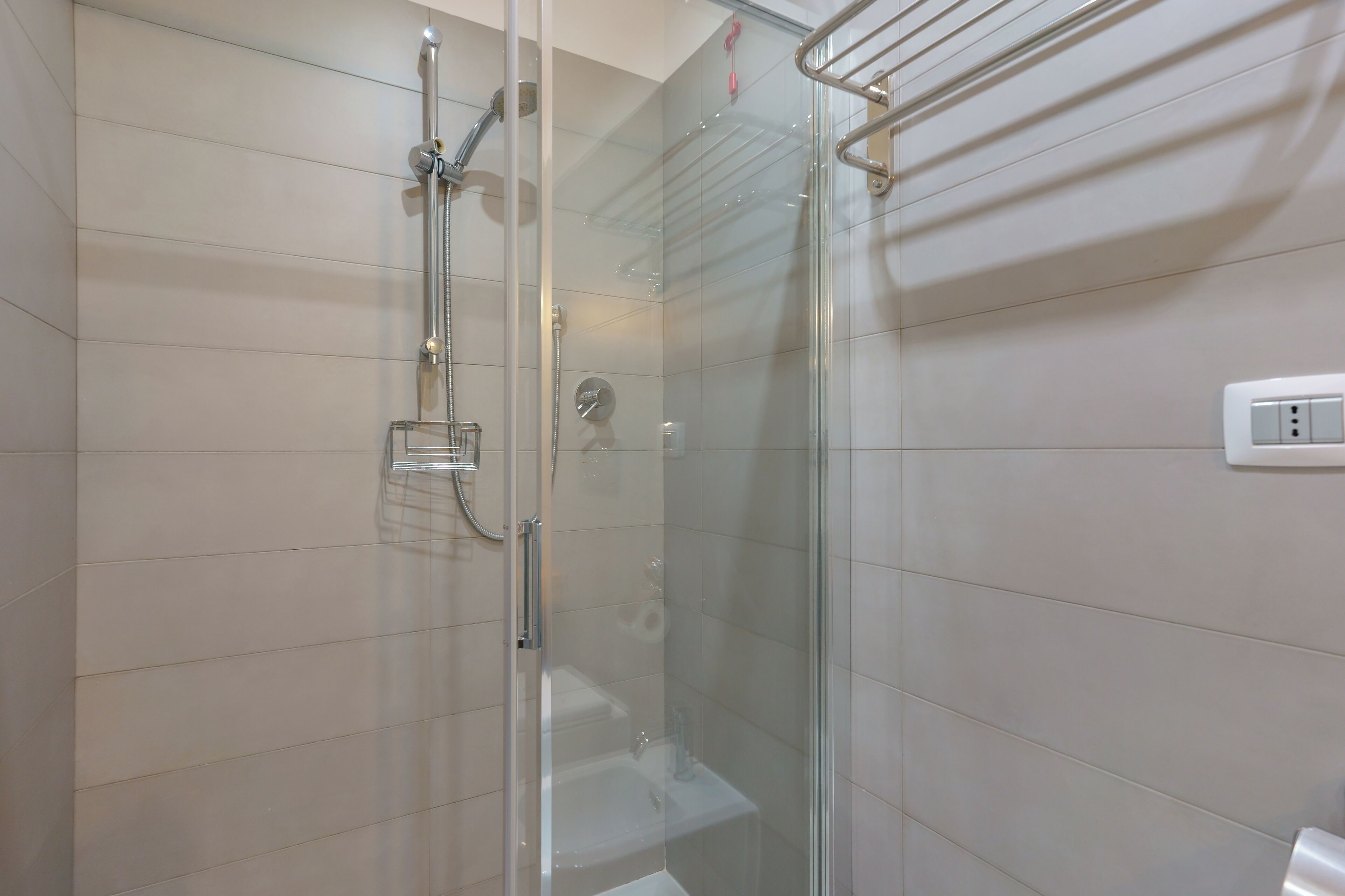 Une douche fermée par des parois en verre, dotée d’un pommeau de douche à main, d’un robinet mural et d’un receveur de douche en verre.