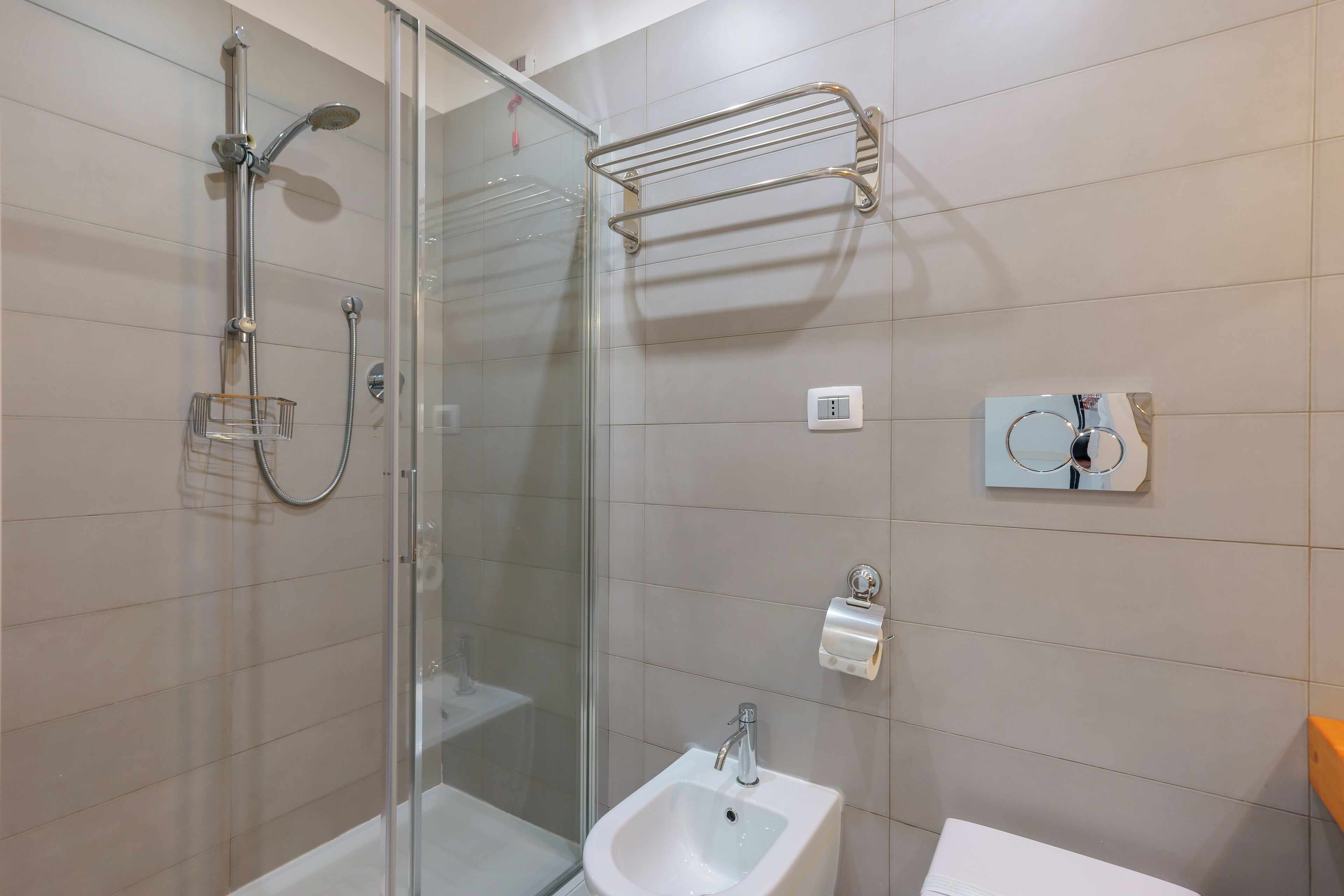 Un baño moderno con cabina de ducha de vidrio, lavamanos pedestal y un perchero para toallas.