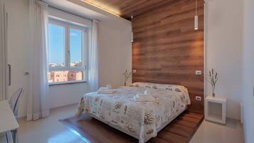A modern bedroom with a wooden ceiling, a large bed with a patterned bedspread, a bedside table with a plant, and a window with curtains.