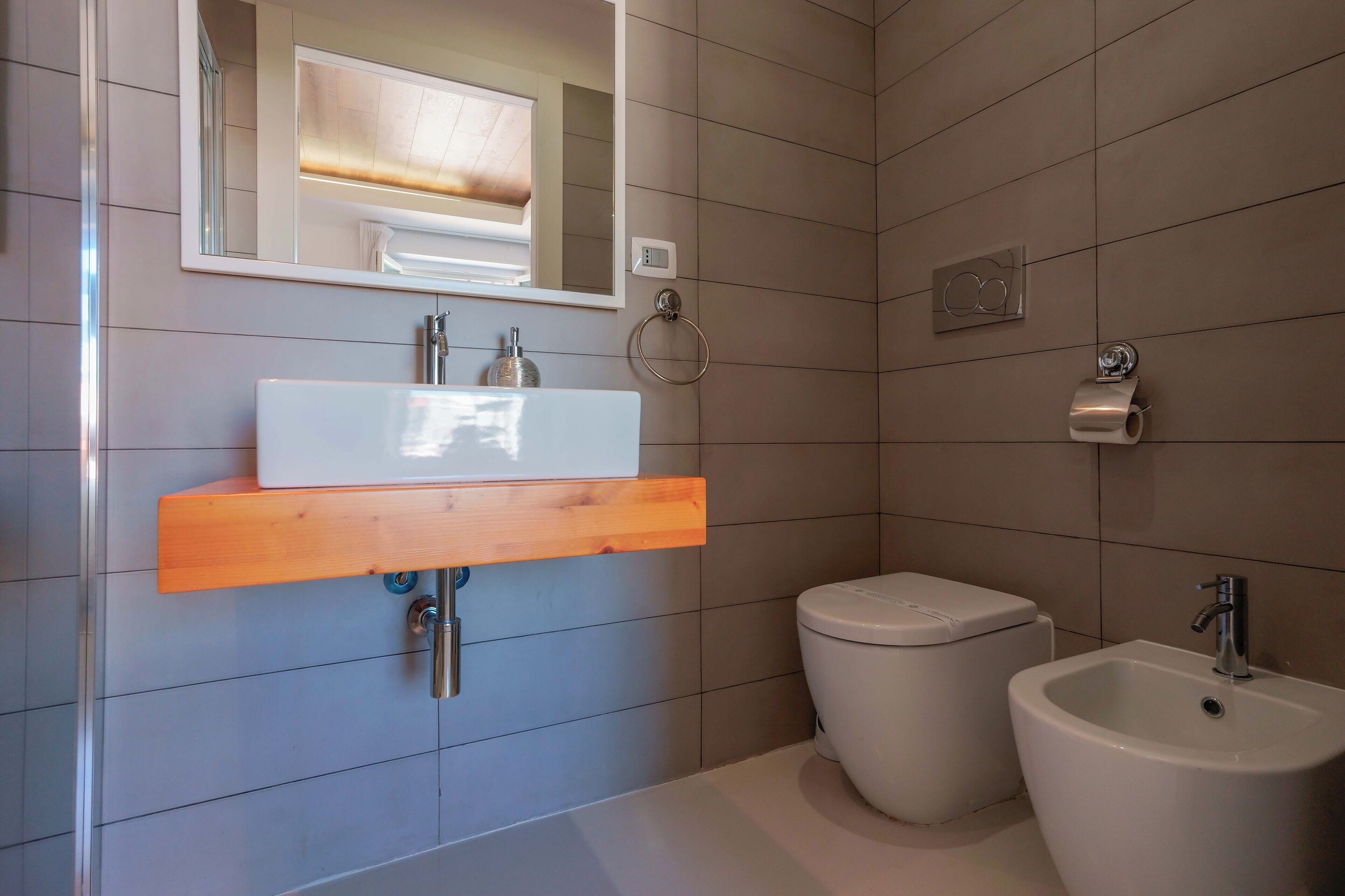 Une salle de bain moderne avec un lavabo blanc, un meuble-lavabo en bois, des toilettes et un bidet.