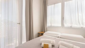 A hotel room with a bed, two pillows, a small table, and a window with curtains.
