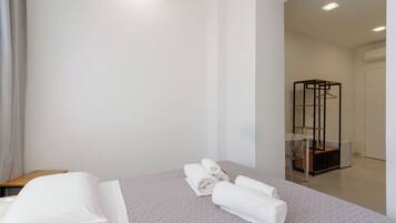 A hotel room with a neatly made bed, a small wooden table, and a metal-framed wardrobe.