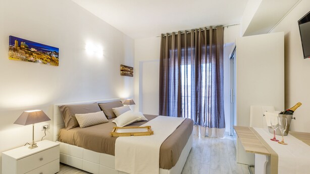 Una habitación de hotel moderna con cama, mesita de noche, lámpara y una botella de champán.