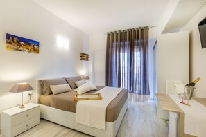 Moderni hotellihuone, jossa on sänky, yöpöytä, lamppu ja pullo samppanjaa.