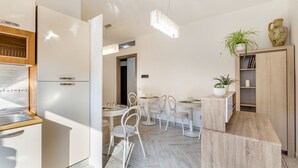 Una cocina moderna con armarios blancos, una zona de comedor con mesas y sillas redondas, y un suelo con estampado de espiga.