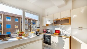 Una cocina moderna con armarios blancos, horno empotrado y una ventana grande con vistas a una zona residencial.