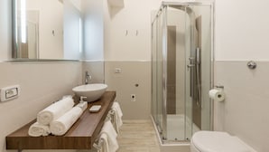 Un baño moderno con tocador de madera, un espejo grande, cerramiento de ducha de vidrio y un inodoro blanco.