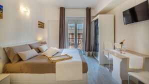 Habitación de hotel moderna con cama, mesita de noche, televisión y balcón con cortinas.