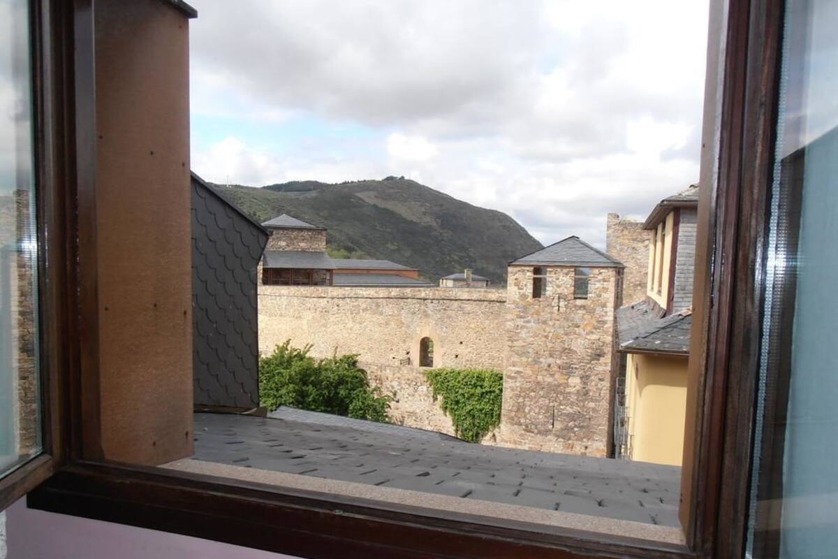 Vista des d'una finestra amb una construcció de pedra i una muntanya al fons.