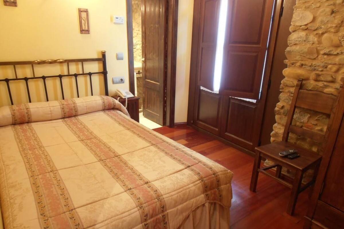 Un dormitori amb un llit gran, sòl de fusta, paret de pedra i una taula petita amb un telèfon.