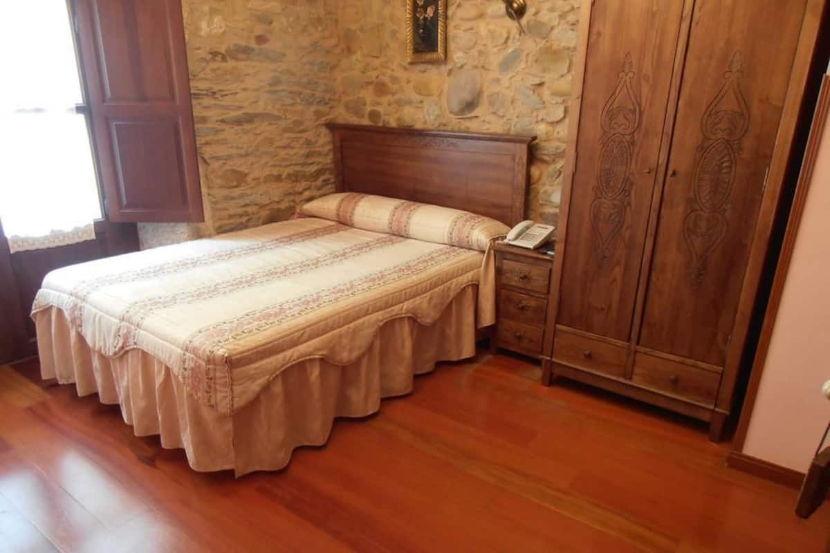 Un dormitori amb un llit de fusta, una paret de pedra i un armari de fusta.