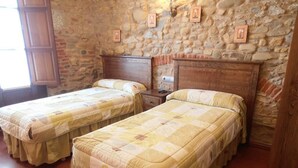 Ein Zimmer mit zwei Betten, Holz-Kopfteilen, einer Steinwand und einem Holzschrank.