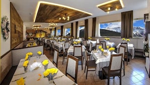 A restaurant with multiple tables set for dining, featuring yellow flowers and white tablecloths. - Hotel Pian Castello (Andalo)